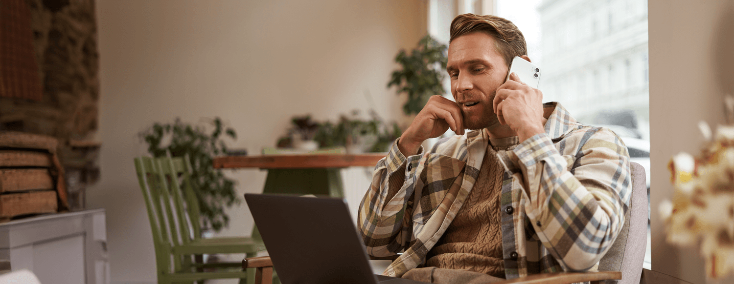 young-man-looking-website-laptop-calling-enquire-about-product-order-something-online-business-professional-sitting-cafe-working-online-talking-smartphone_with_bgc